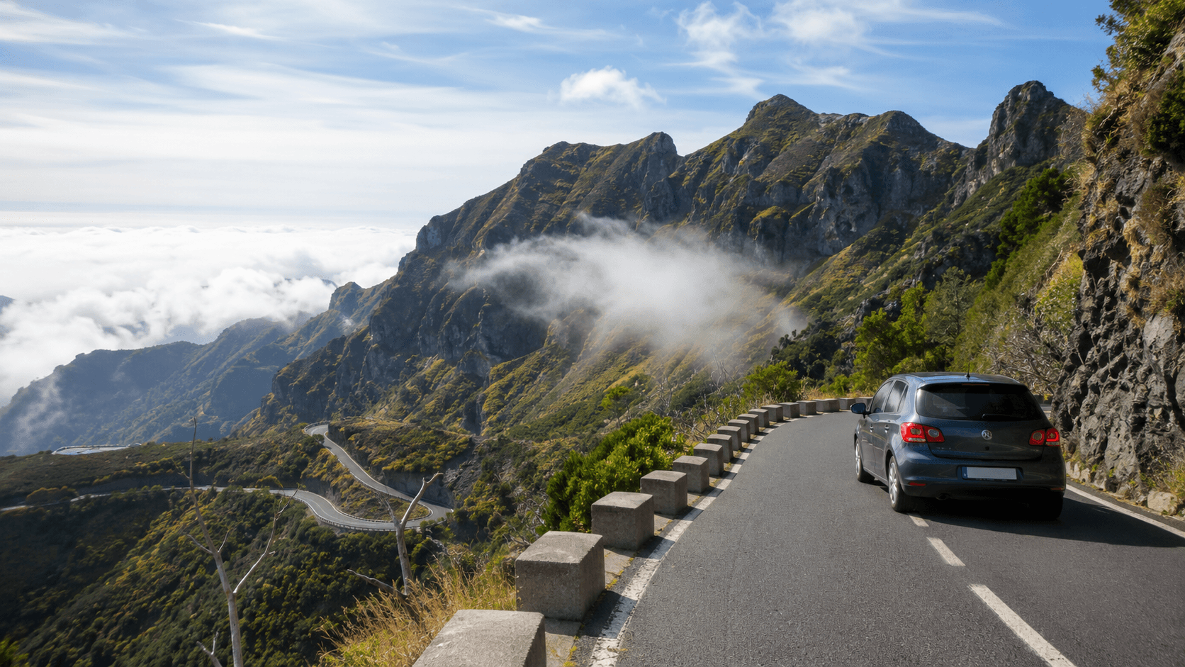 Winding mountain road in Madeira with a compact car and clouds